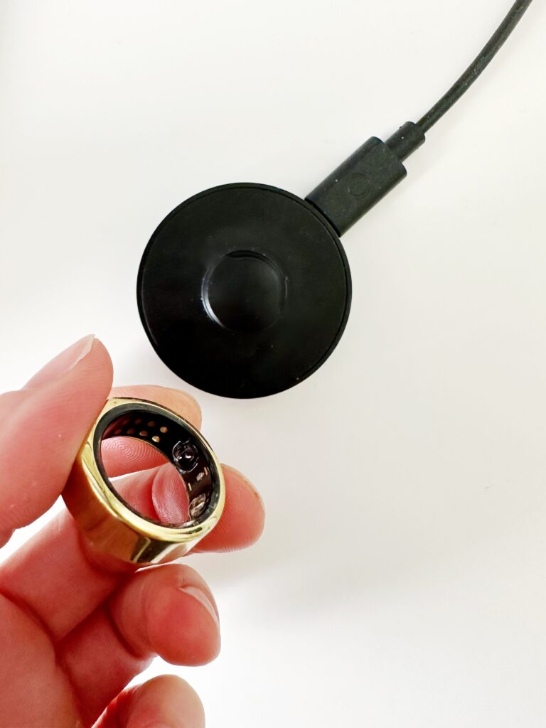 woman holding oura ring next to charger