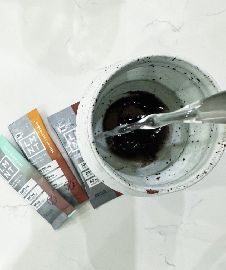 pouring hot water in a mug with LMNT chocolate flavor packets next to mug